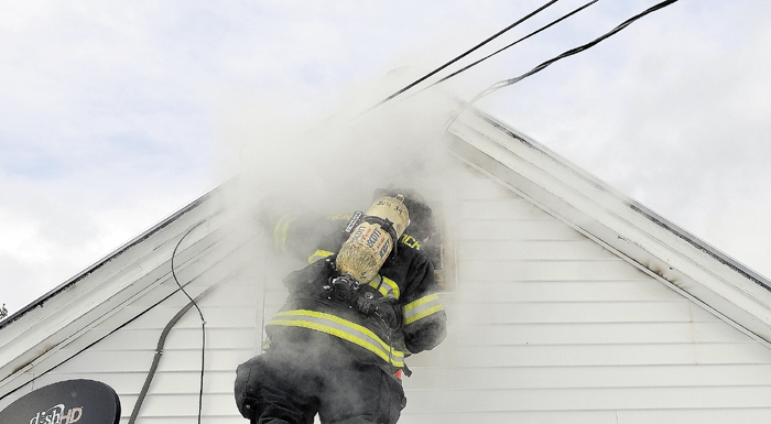 Nicholas Quimby, a firefighter with Norridgewock cuts a hole in the wall while battling a house fire at 567 Norridgewock Rd in Fairfield Wednesday afternoon.