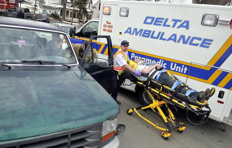 A Delta Ambulance emergency medical technician transports a victim of a two-car accident to a waiting ambulance, as a Waterville firefighter talks to Albert DiPietro, 28, of Richmond, seated in his truck, on Upper Main Street Friday afternoon. DiPietro's truck struck the rear end of a car, sending two adults and two children to MaineGeneral Medical Center's Thayer Campus for neck and back pain and minor injuries.
