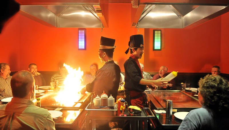 Chef Jerry Lin, left, heats up the hibachi as chef Ricky Huang squirts sake in to diners' mouths during an entertaining exhibition of culinary skills for a group of diners at Mirakuya Steak House in Waterville Wednesday night.