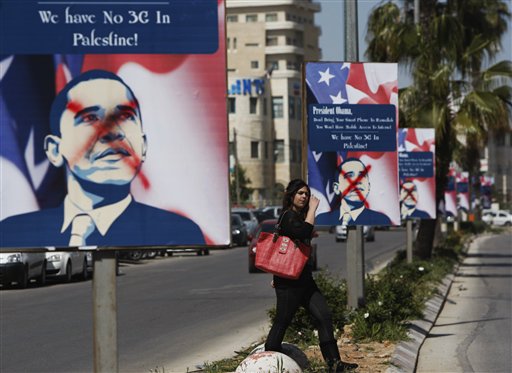 A Palestinian woman walks past vandalized posters showing President Barack Obama in the West Bank city of Ramallah on Thursday.