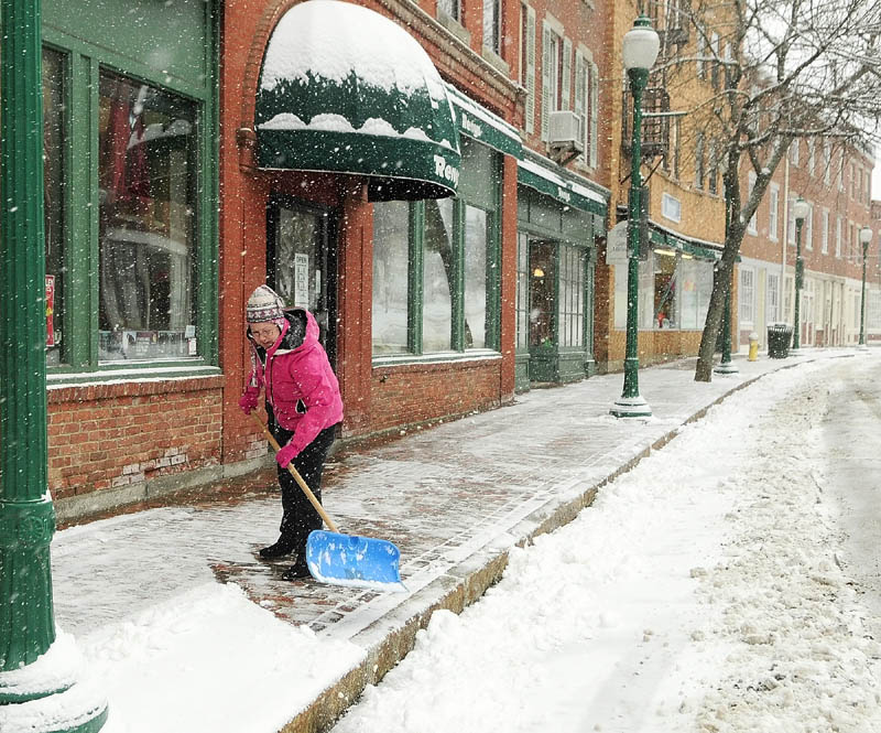 April Hall shovels snow from a late winter storm in front of the Reny's store, where she works, on Tuesday in Gardiner.
