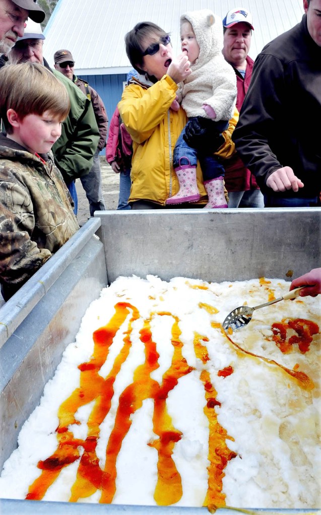 Lisa Wheeler gives her granddaughter, Lilly Wheeler, a taste of maple taffy, made by pouring hot maple syrup over snow, at Strawberry Hill Farms in Skowhegan, during the statewide Maine Maple Sunday event.