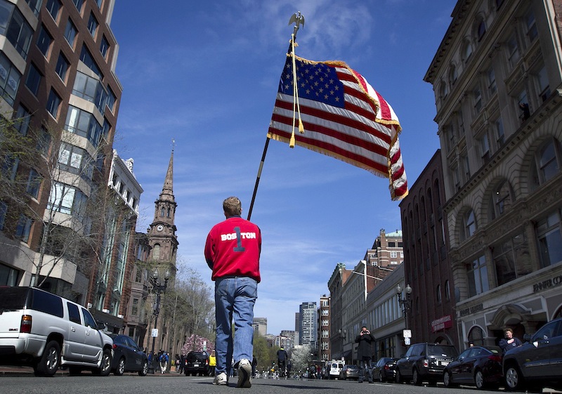 Lt. Mike Murphy of the Newton, Mass., fire dept., carries an American flag down the middle of Boylston Street after observing a moment of silence in honor of the victims of the bombing at the Boston Marathon near the race finish line, Monday, April 22, 2013, in Boston, Mass. A fund created to benefit the victims of last week's Boston Marathon bombings has generated $20 million, said state officials, who vowed to distribute the money by the Fourth of July. (AP Photo/Robert F. Bukaty)