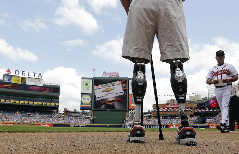 In this Monday, May 28, 2012 file photo, U.S. Army Capt. Dan Berschinski, foreground, uses prosthetic legs to stand on the field before a baseball game between the St. Louis Cardinals and Atlanta Braves in Atlanta. Nearly 2,000 American troops have lost a leg, arm, foot or hand in Iraq or Afghanistan, and their sacrifices have led to advances in the immediate and long-term care of survivors, as well in the quality of prosthetics that are now so good that surgeons often chose them over trying to save a badly mangled leg. (AP Photo/David Goldman)