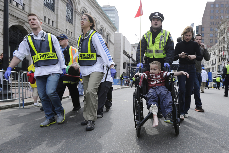 A Boston police officer wheels in injured boy down Boylston Street as medical workers carry an injured runner following an explosion during the 2013 Boston Marathon in Boston, Monday, April 15, 2013. Two explosions shattered the euphoria at the marathon's finish line on Monday, sending authorities out on the course to carry off the injured while the stragglers were rerouted away from the smoking site of the blasts. (AP Photo/Charles Krupa)
