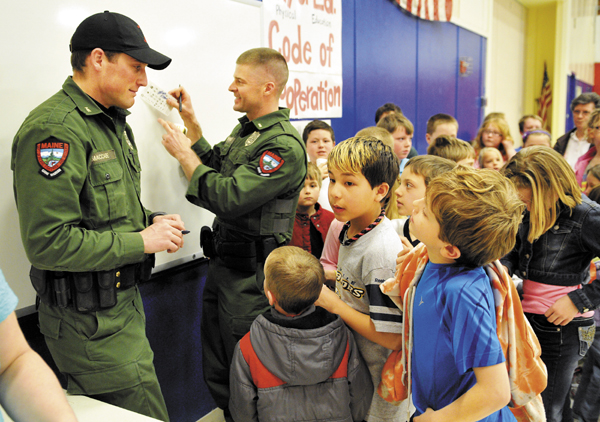 Game Wardens Kris MacCabe, left, and Lt. Shon Theriault sign autographs for students and faculty Monday during a visit to the Belgrade Central School.