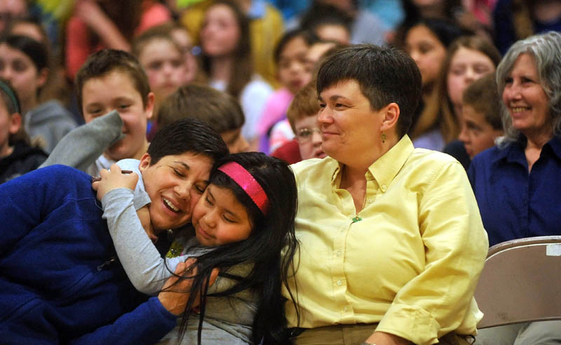 Marisa Weinstein, left, music teacher at Warsaw Middle School, gets a hug from her daughter, Marta, 8, center, and partner, Marilyn Buzy, right, after she was presented the Maine Music Educators Association Educator of the Year award during a surprise assembly at the Pittsfield school on Tuesday.