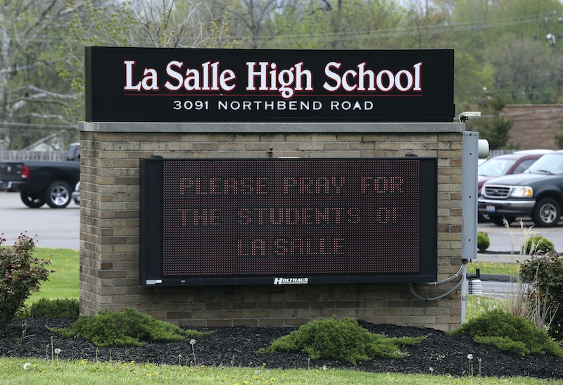 A sign posted in front of La Salle High School, Monday, April 29, 2013, in Cincinnati, asks for prayer after a student pulled out a gun and shot himself in a classroom. La Salle High School west of Cincinnati was locked down until after police arrived and determined there was no threat to other students or staff. A University of Cincinnati Medical Center spokeswoman reported the student's condition as critical Monday afternoon, about six hours after the shooting. (AP Photo/Cincinnati Enquirer, Cara Owsley)