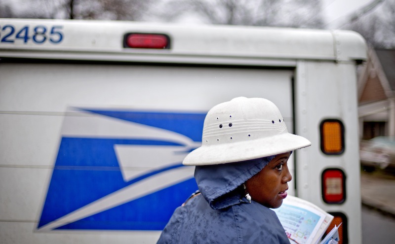 In this Feb. 7, 2014 file photo, U.S. Postal Service letter carrier Jamesa Euler, delivers mail in the rain in the Cabbagetown neighborhood, in Atlanta. The U.S. Postal Service says it will delay plans to cut Saturday mail delivery because Congress isn't allowing the change. The Postal Service said in February that it planned to cut back in August to five-day-a-week deliveries for everything except packages, as a way to hold down losses. (AP Photo/David Goldman)