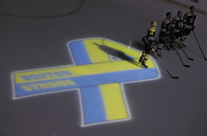BOSTON STRONG: Boston Bruins players, including defenseman Dennis Seidenberg (44), stand next to a ribbon projected onto the ice at TD Garden on Wednesday in Boston during a pregame ceremony in the aftermath of Monday’s Boston Marathon bombings. TD Garden