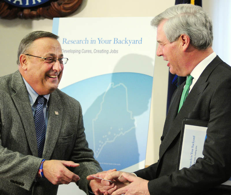Gov. Paul LePage, left, presents an "Open for Business" business card to PhRMA CEO John Castellani at a news conference Friday at the State House in Augusta. A new report says the more than 550 clinical trials of new medicines in Maine since 1999 support thousands of jobs and millions of dollars in federal and state taxes.
