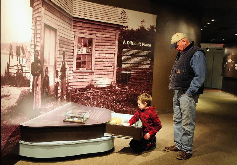 Ciaran Seltsman, 9, of Augusta, left, and his grandfather, Robert Seltsman, of Leeds, look at items in a drawer on Thursday in the "Malaga Island, Fragmented Lives" exhibition at the Maine State Museum in Augusta.