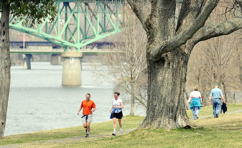 Runners and walkers make their way along the banks of the Kennebec River on the Augusta Greenway trail, on the Kennebec arsenal grounds, on Friday.