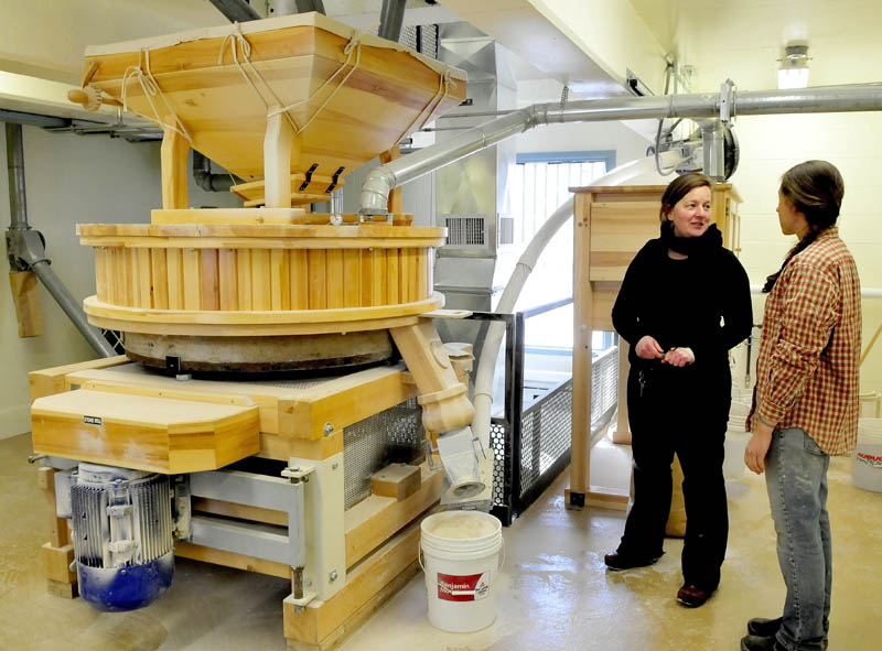 Amber Lambke, left, owner of Maine Grains, and head miller Julie Zavage discuss an order of flour being ground in the stone mill, left, at the Somerset Grist Mill in Skowhegan on Thursday.