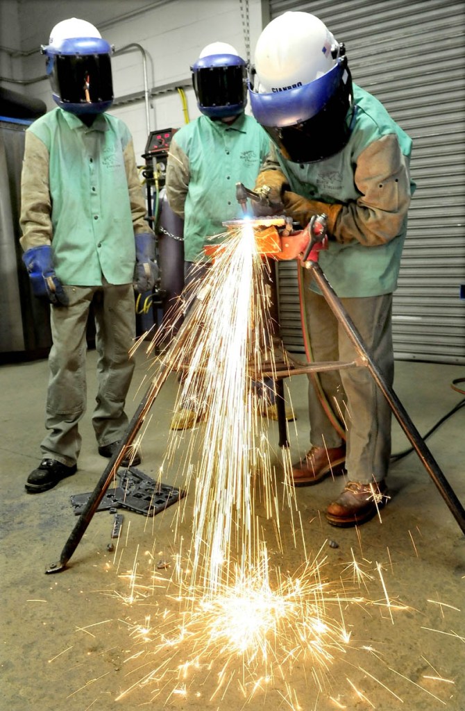 Skowhegan Area High School student Sarah Finnemore uses a cutting torch to cut steel at the Cianbro company welding training center. Waiting their turn are Cody Bailey, left, of Carrabec High School and Devon Blodgett of Valley High School.