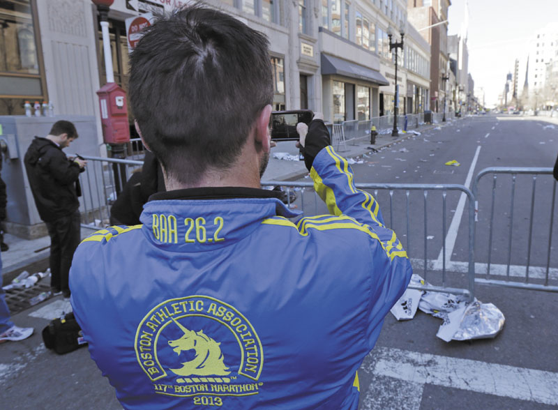 Paul McRae, a native of New Zealand now living in Jacksonville, takes a photograph of an empty Boylston Avenue near the Boston Marathon finish line, in Boston, Tuesday, April 16, 2013. Three people and more than 140 were injured when bombs exploded seconds apart close to the finish line on Monday. McRae finished the race before the explosions. (AP Photo/Charles Krupa)