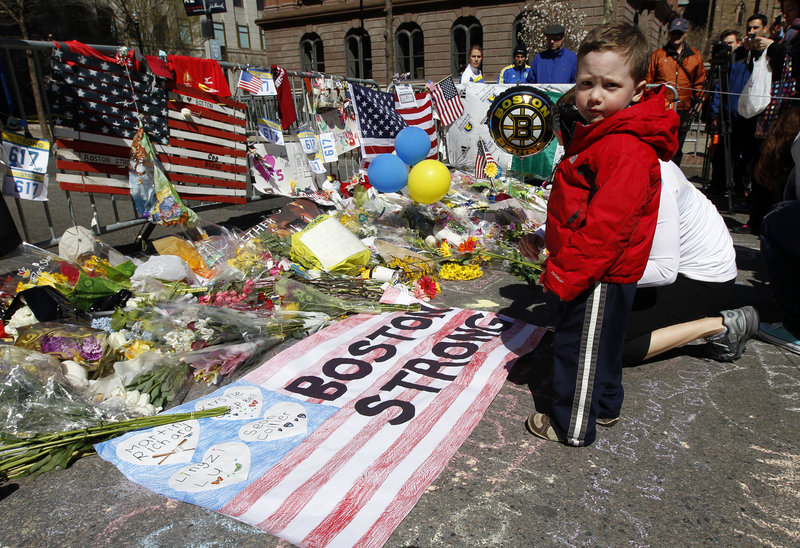 Two-year-old Wesley Brillant of Natick, Mass., stands Sunday in front of a memorial to the victims of the Boston Marathon bombings on Boylston Street. Officials plan to hold a moment of silence Monday at 2:50 p.m., the time the first bomb went off.