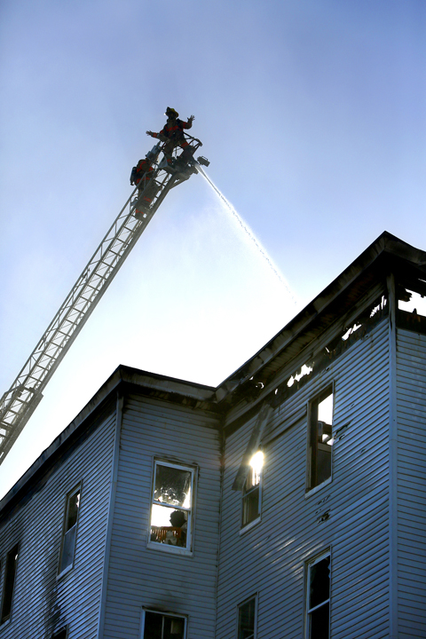 Firefighters spray water on the roof of a vacant apartment building on Bartlett Street in Lewiston on Monday.