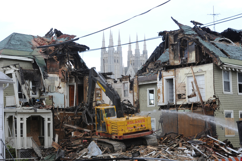 A demolition crew tears down 80-82 Pine St. in Lewiston on Friday while Maine Sen. Angus King tours the site with city officials. In the background are the spires of the Basilica of Saints Peter and Paul. King
