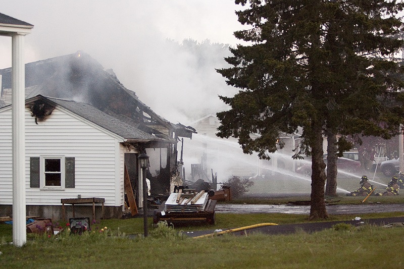 Firefighters put out the blaze set by Saco homeowner Charles Scontras during a standoff with police at his home Saturday. Neighboring homes were doused to keep the fire from spreading.