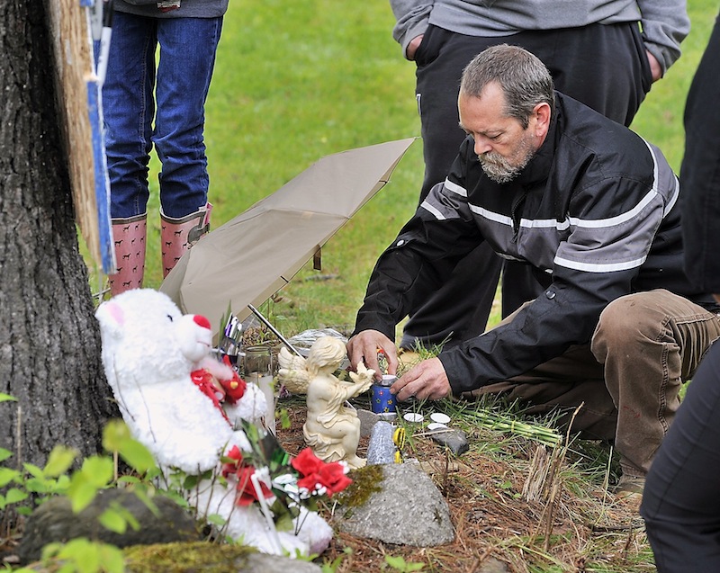 Timothy Munson, a neighbor and friend of Nichole Cable’s family, relights candles Tuesday on the memorial for the 15-year-old at the base of the dirt road where she lived in Glenburn.