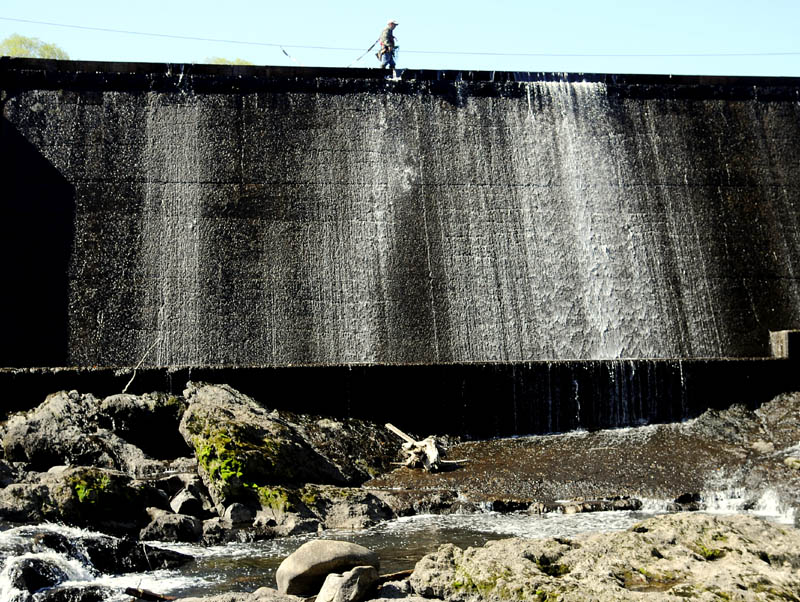 Jeremy Gorman walks on the lip of the American Tissue Dam Tuesday on Cobbossee Stream in Gardiner while deploying safety barrels. Wearing a safety harness and hooked onto a cable, Gorman said the barrels were deployed in the current to deter boaters from approaching the 20 foot drop off at the hydro-electric dam.
