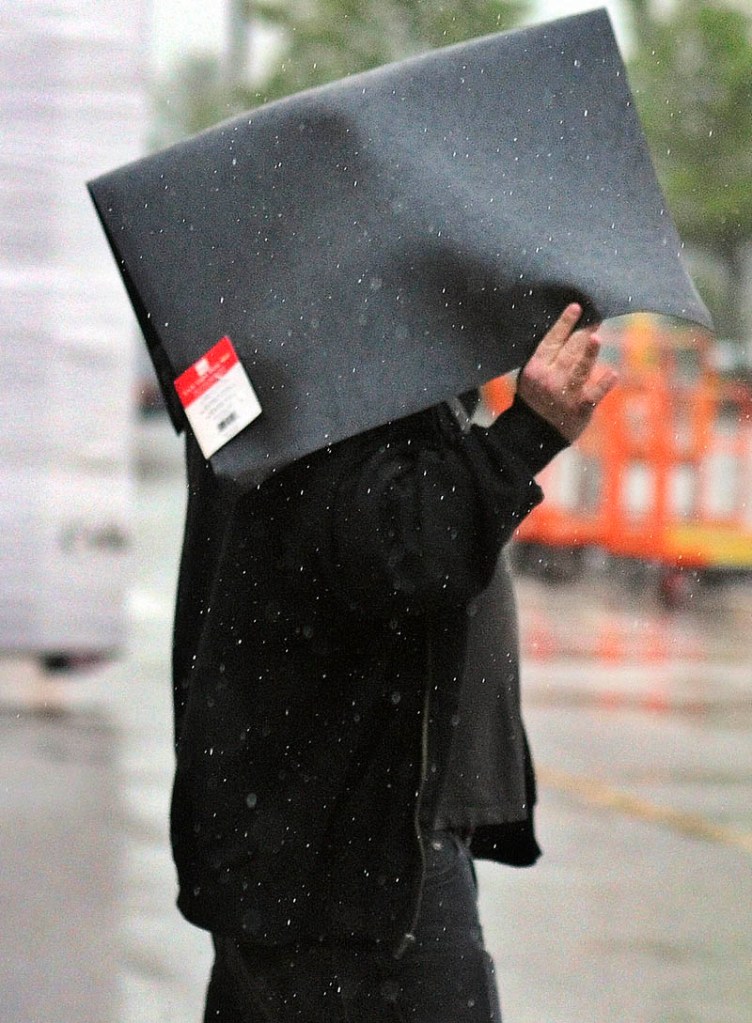James Dunlop, of Richmond, holds a floor mat he purchased over his head Wednesday while exiting Home Depot in Augusta in pouring rain. The clouds are expected to dissolve by Thursday and temperatures may climb in to the 90s by Friday, according to forecasts. Dunlop said the mat will be placed in front of the sink at his home.
