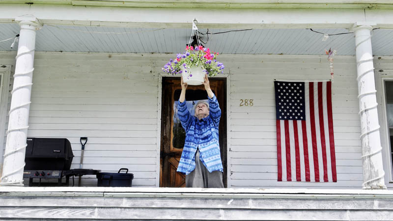Ann Gleason hangs a flower basket Tuesday on the porch of her Manchester home. Blue skies prevailed as Gleason watered her plants. The weather is forecast to remain mild with clear skies through the remainder of the week.