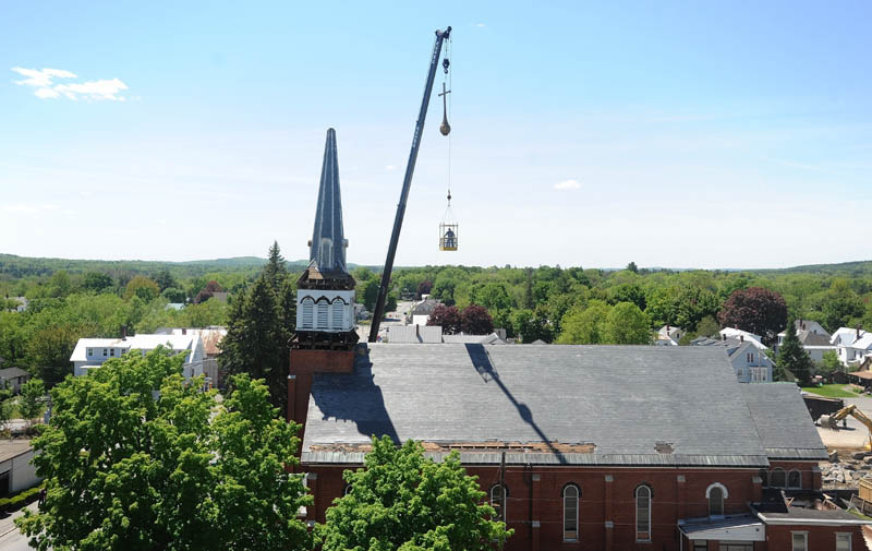 The cross that stood atop the steeple of Saint Francis de Sales Catholic Church in Waterville is hoisted over the church as the steeple is removed by sections during demolition on Tuesday.