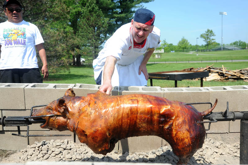 Chef Mikael Andersson checks the temperature of the pig with the help of Chef Ramon Managad, left, during preparations for a pig roast in honor of Colby College food service workers employed by Sodexo, at Colby College on Friday. Sodexo annually throws a pig roast party for its employees.