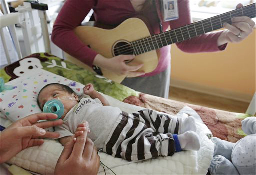 Music therapist Elizabeth Klinger, right, plays guitar and sings for Augustin as he grips the hand of his mother, Lucy Morales, in the newborn intensive care unit at Ann & Robert H. Lurie Children's Hospital in Chicago recently.