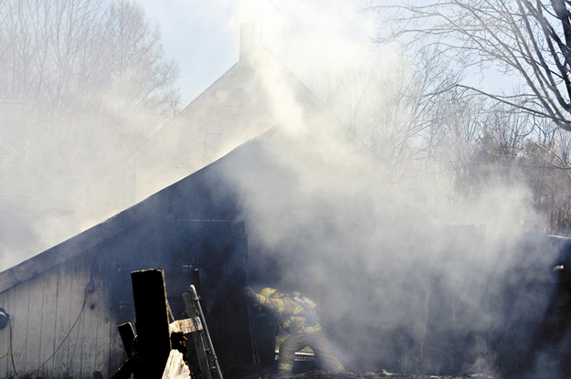 A firefighter pops open the door to a barn that burned Wednesday with a garage attached to a home in Readfield. Firefighters from several communities were able to contain the blaze from heavily damaging the home, according to Wayne Deputy Fire Chief Brian Roche.