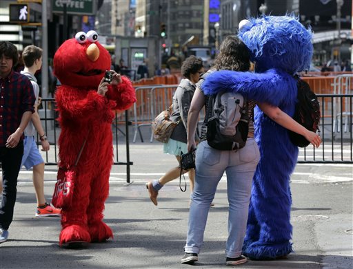 An Elmo character, left, uses a woman's camera to photograph her with a Cookie Monster character in New York's Times Square recently. A string of arrests in the last few months has brought unwelcome attention to the growing number of people, mostly poor immigrants, who make a living by donning character outfits, roaming Times Square and charging tourists a few dollars to pose with them in photos.