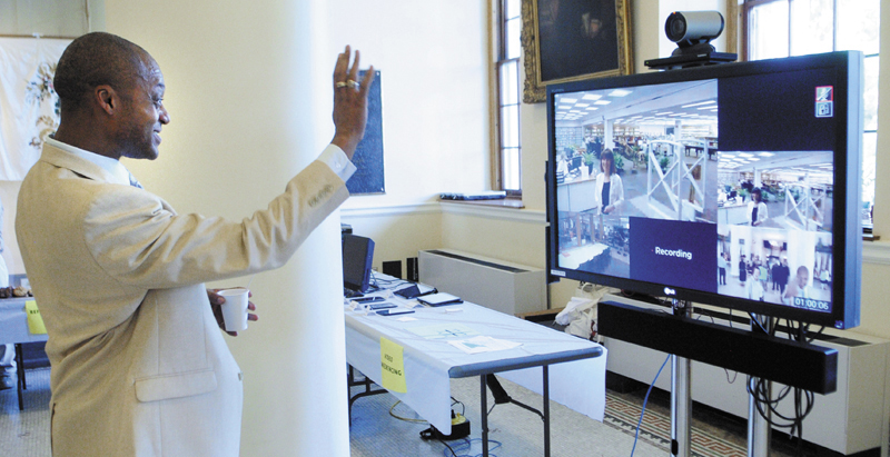 Rep. Craig Hickman, D-Winthrop, waves through a video conferencing monitor to Maine State Library employee Jill Sampson, who was watching an event in the State House's Hall of Flags, held to celebrate the completion of the Maine State Library's $1.9 million Broadband Technology Opportunity Program, on Friday.