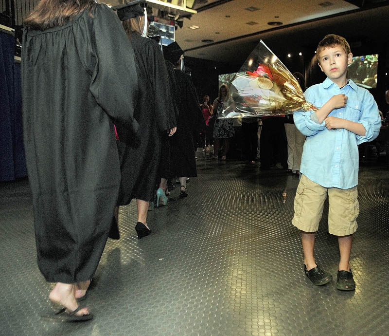 As a line of graduates passes, John Rice, 7 of Damariscotta, looks for his mother Susanna Norwood-Burns to give her a bouquet at the start of University of Maine at Augusta graduation.