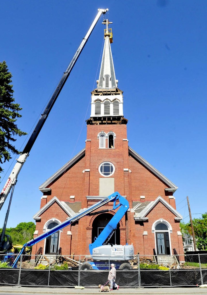 A pedestrian walks past the St. Francis de Sales Catholic Church in Waterville as the cross and steeple are being removed on Tuesday. The church is being torn down and a housing complex will be built at the location.