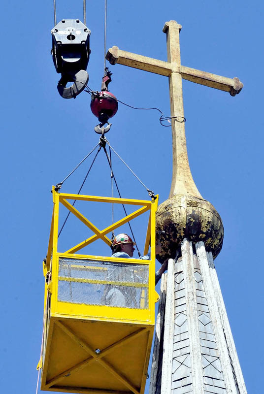 Gene Green works 60 feet above the ground, in a cage suspended from a crane, as he labors to sever the cross from the steeple atop St. Francis de Sales Catholic Church in Waterville on Tuesday.