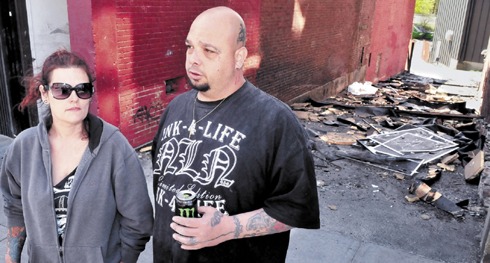 Mona and Bill Juliano, owners of Ink-4-Life tattoo parlor, speak Monday outside an alley littered with debris from the Waterville apartment building fire that destroyed their business and left tenants homeless on Friday. The Julianos are planning to relocate across Main Street in the former Levine's building.
