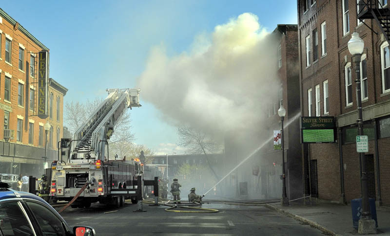 Firefighters spray water on a building on fire in downtown Waterville on Friday afternoon. The block is between Spring and Silver streets.