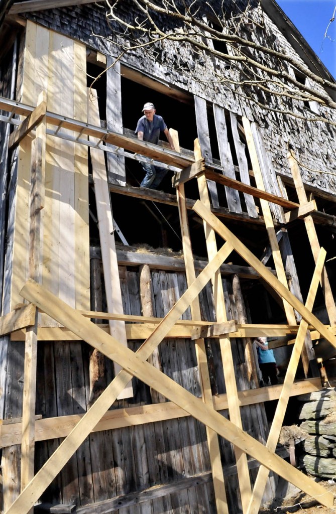 David Frederick lifts a long board into place while repairing his barn in Norridgewock recently. His wife Brenda can be seen at lower right pulling the rope that helped lift the heavy timber.