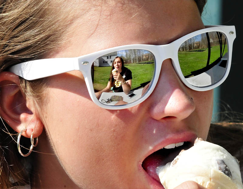Maggie Feine enjoys an ice cream cone with her friend, Kayla Turner, seen in the reflection of Feine's sunglasses, at North Street Dairy Cone in Waterville on a warm Thursday afternoon.
