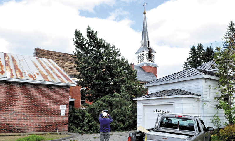 The second of two spruce trees begins to fall beside the St. Francis de Sales Catholic Church in Waterville on Monday. The church will be taken down this summer to make way for a housing project. The parish building, at left, and the building on the right will be torn down later this week.