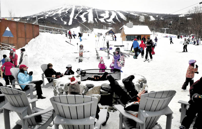Skiers and snowmobilers relax around an outdoor fire at the base lodge at Sugarloaf.
