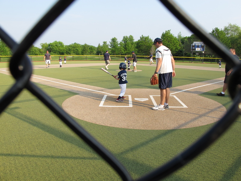 A young batter takes a swing as a father who is a coach supervises at a youth baseball game in Buffalo Grove, Ill., on Monday. Earlier in the month, park district officials in the Chicago suburb posted signs asking parents to behave and keep the games in perspective.