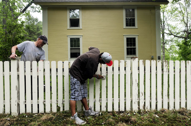 Doug Rooks, left, and his son, Emlyn Rooks-Hughes, scrape down the picket fence at their West Gardiner home on Monday. The duo planned to apply a new coat of paint to the border around their farmhouse, erected in 1805.