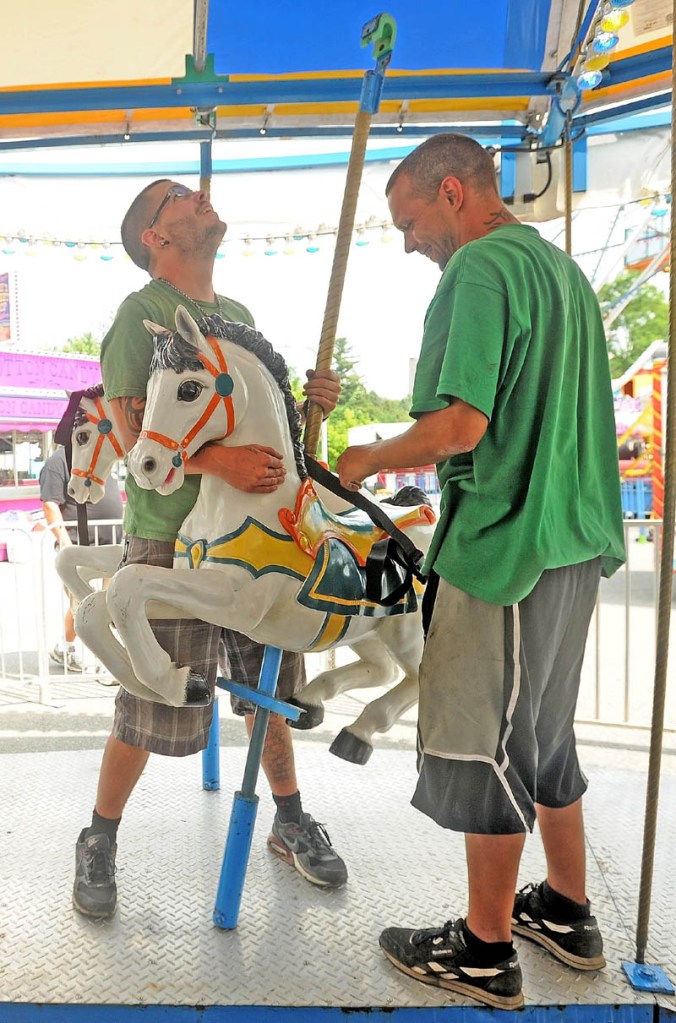 Adam Trott, 25, left, and Tim Siwek, 32, right, install a horse on the merry-go-round at the East Coast Midways carnival in Fairfield on Tuesday.