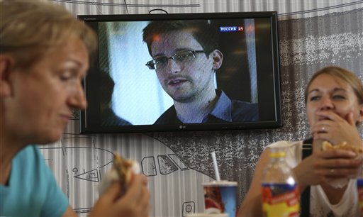 Transit passengers eat at a cafe with a TV screen with a news program showing a report on Edward Snowden, in the background, at Sheremetyevo airport in Moscow Wednesday.