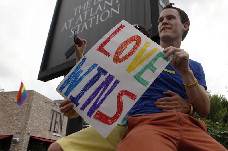 Daniel Hicks sits on a pillar with his boyfriend to watch the local crowd celebrate the U.S. Supreme Court's rulings on two landmark gay rights cases surrounding same-sex marriage on the corner of Piedmont Ave. and Tenth Street in Midtown, Wednesday, June 26, 2013, in Atlanta. (AP Photo/Jaime Henry-White)