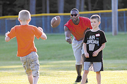 HERE IT IS: Former New England Patriots player Eric Alexander tosses a football to 8-year-old Trent Worcester of Madison while running the annual Central Maine Football Clinic on Friday in Waterville. Looking on is Jayden Meader, 7, of New Sharon, right. The clinic will continue from 9 a.m. to 3 p.m. today at Rummel Field off West River Road.