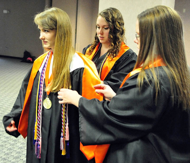 Salutatorian Hannah Morgan, left, gets a hand with her regalia from Emily Kobrook, center, and Paige Hinkley, before the Gardiner Area High School commencement ceremony on Saturday at the Augusta Civic Center.